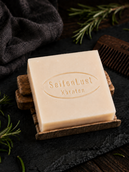 Bartseife „Ritter-Rosmarin“ von SeifenLust® auf einer Holzablage, arrangiert mit Rosmarinzweigen, dunklem Tuch und Bartkamm auf rustikalem Untergrund.